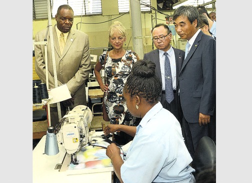 (From left): Executive Director of the HEART Trust/NTA, Dr Wayne Wesley; JPS President & CEO, Kelly Tomblin; Chairman of the JPS, Jin Won Kim; and former president of the Association of Korean residents in Jamaica, Young Ki Moon watch attentively as Shelly-Ann Allen, former HEART trainee now full-time employee of the Garmex HEART Academy, demonstrates how the ‘BannaBag’ is made.